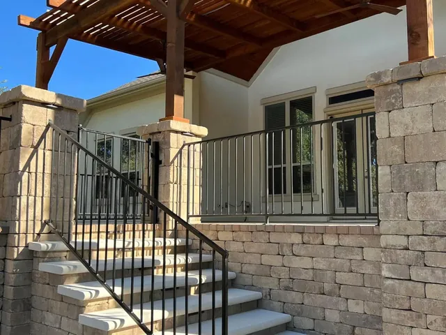 A cedar pergola over limestone steps between stone columns with an iron handrail