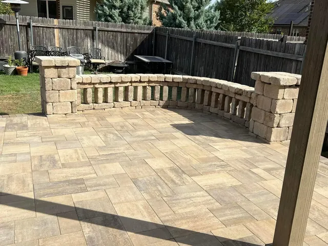 A curved stone seat wall with a flat cap running around a tumbled paver patio