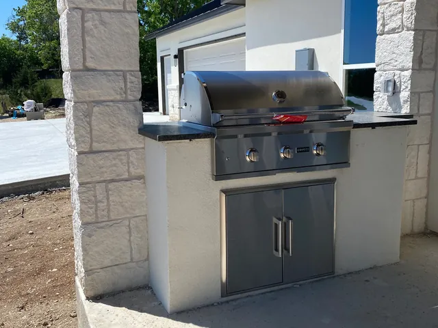 An outdoor kitchen with a built-in stainless grill in a stone and stucco surround