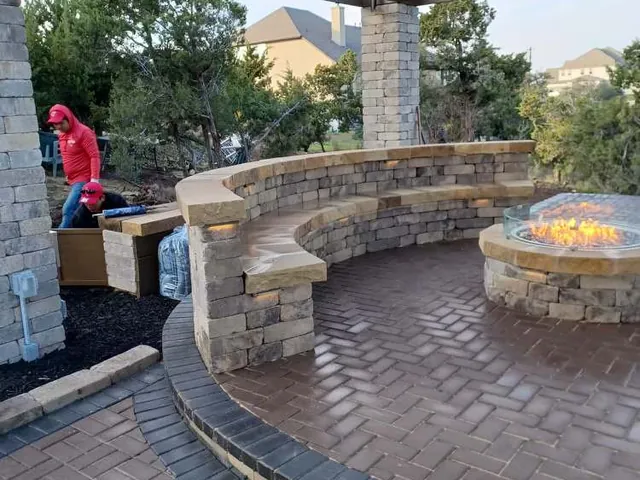 A curved capped seat wall and a fire feature under a pergola on a paver terrace