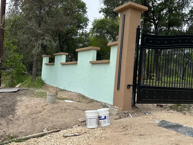 A stucco and stone entry wall with a wrought iron gate across a driveway
