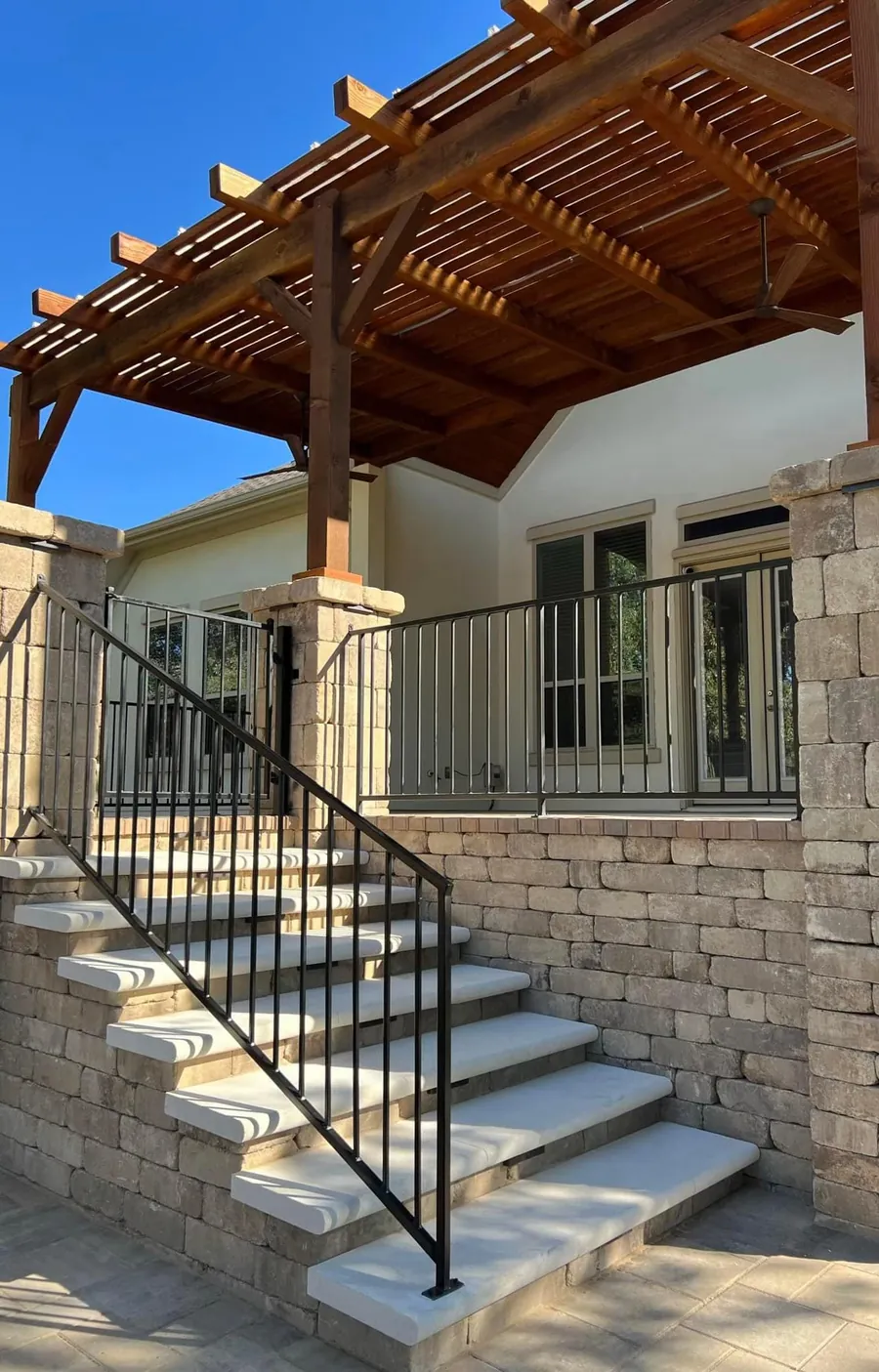 A cedar pergola over limestone steps between stone columns, with an iron handrail