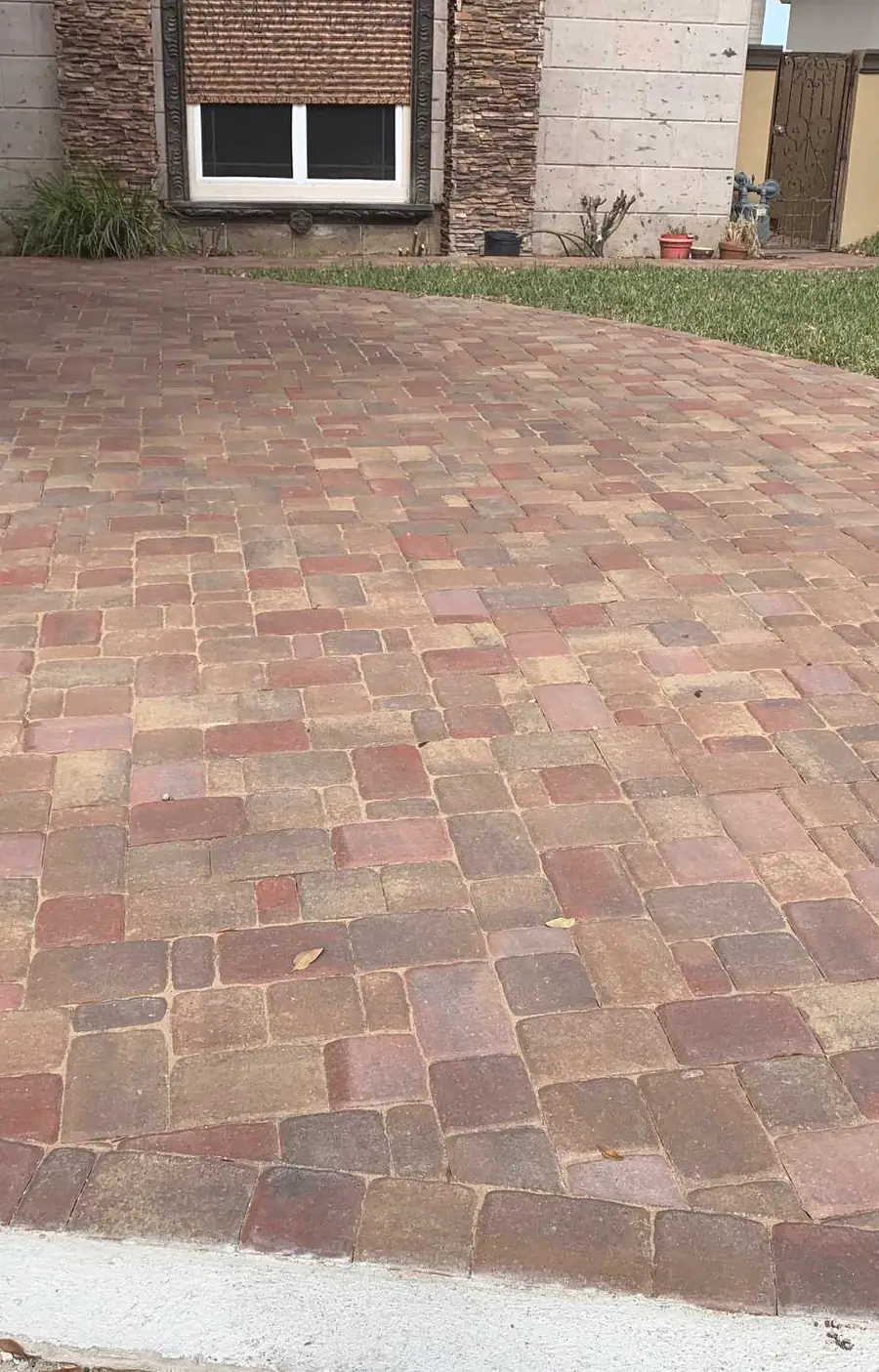 A red and tan tumbled paver driveway curving up to a stone and stucco house
