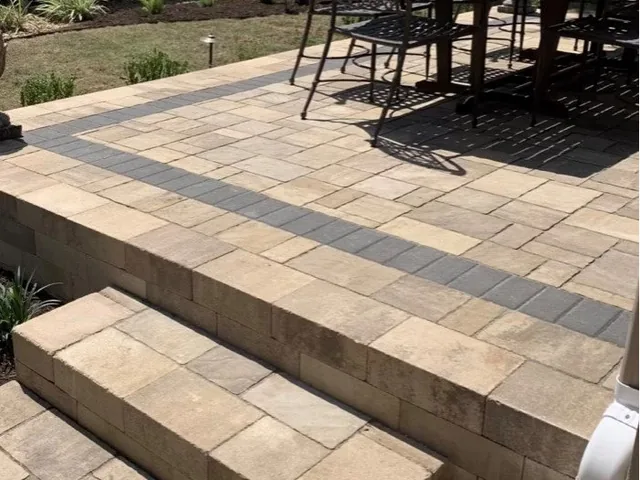 Wide paver steps down from a raised patio, with a dark banded border running through the paving