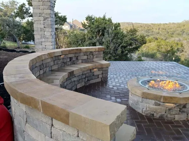 A round fire pit and a curved seat wall on a paver terrace, with Hill Country scrub beyond